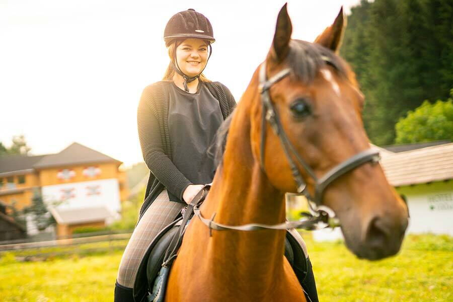 Woman riding a brown horse in front of the Trattlers Hof Chalets in Carinthia.
