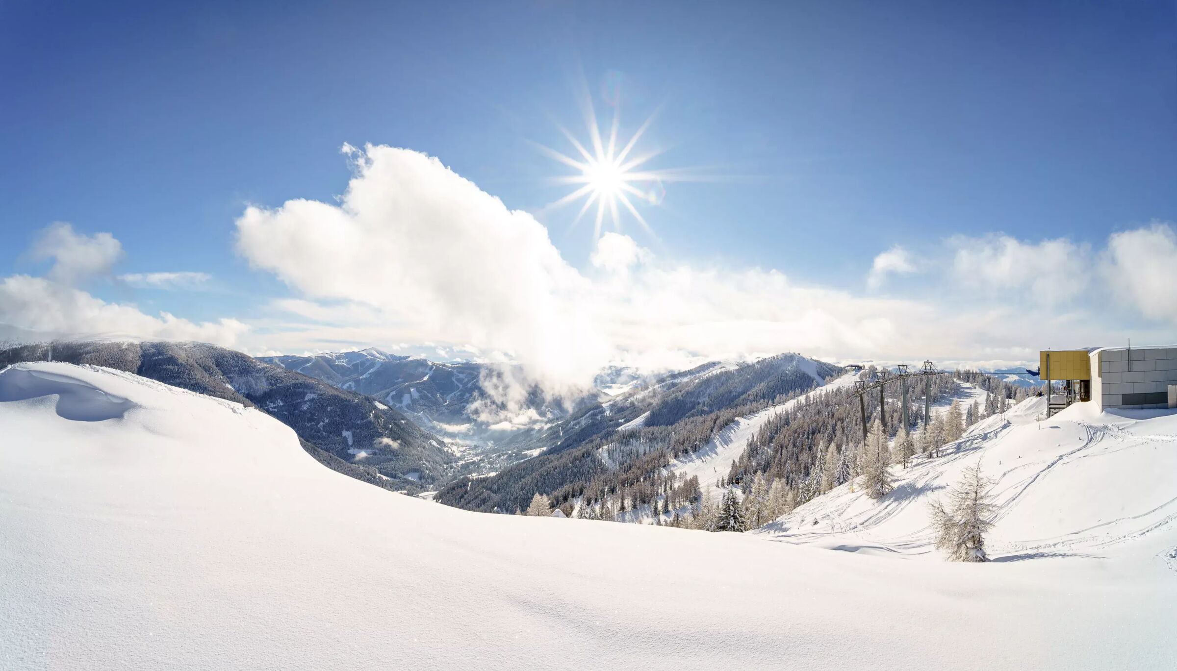 Snow-covered mountains under a bright sky with sun and cloud-covered peaks.
