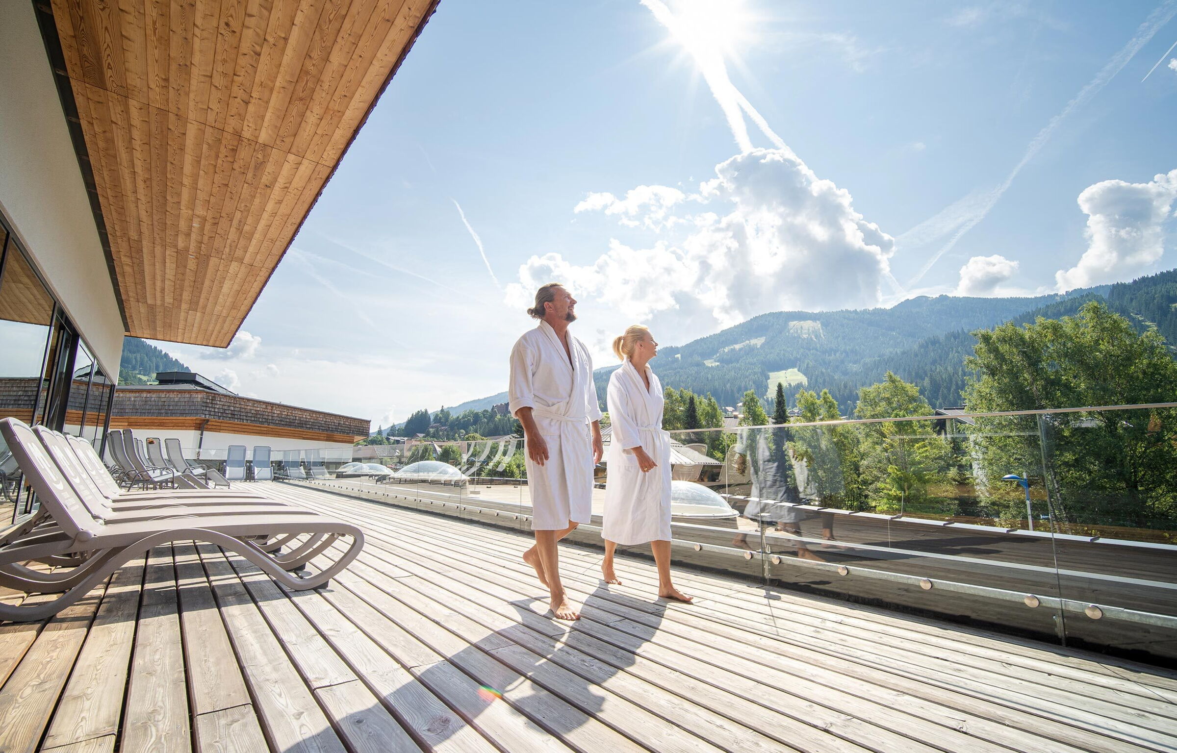 Paar in Bademänteln genießt sonnige Terrasse mit Bergblick in Kärnten.