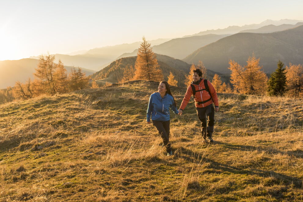 Paar wandert Hand in Hand durch goldene Herbstlandschaft der Nockberge.