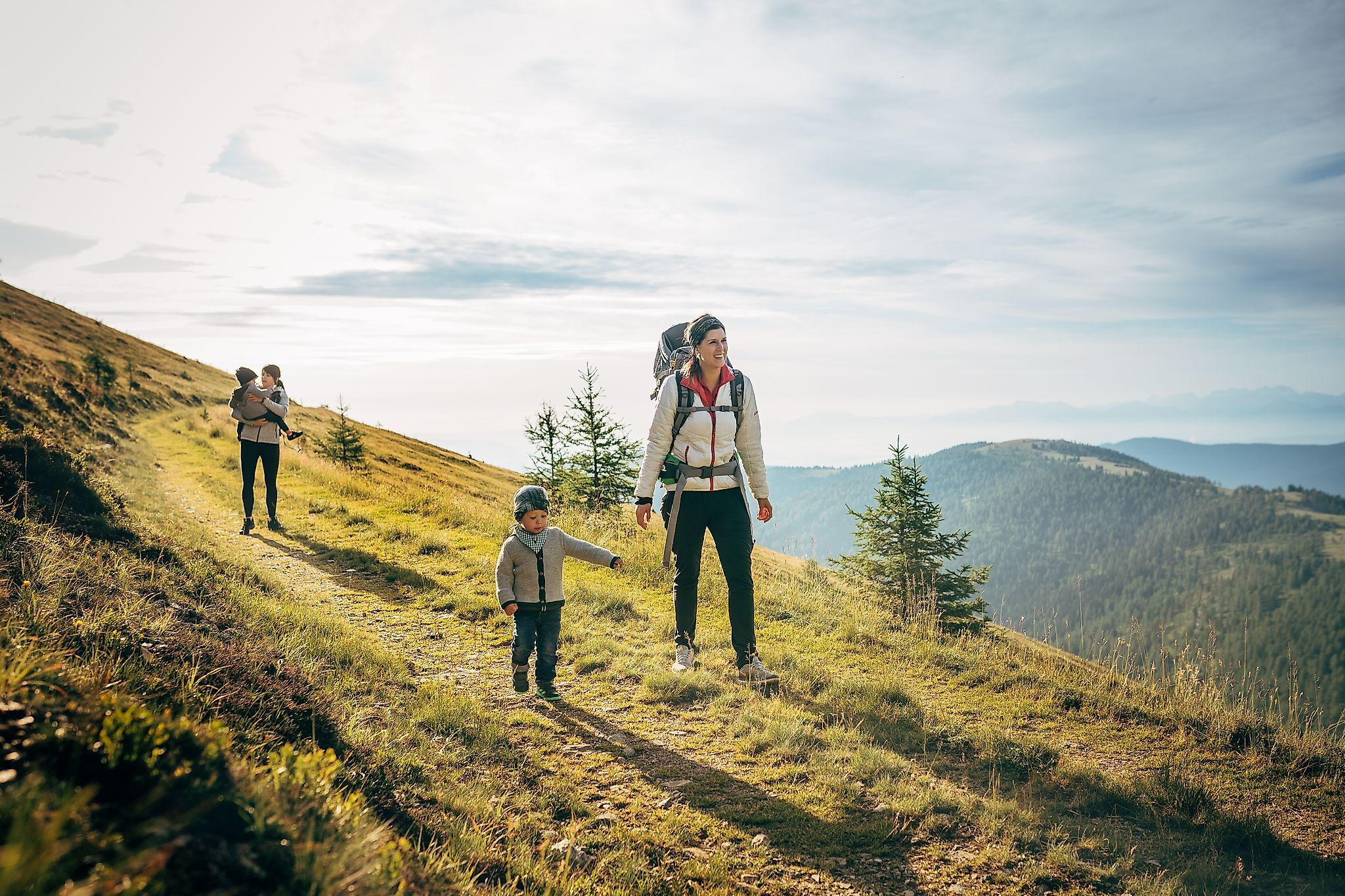 Passeggiate in famiglia lungo un soleggiato sentiero di montagna, circondato da prati verdi e panorami mozzafiato.