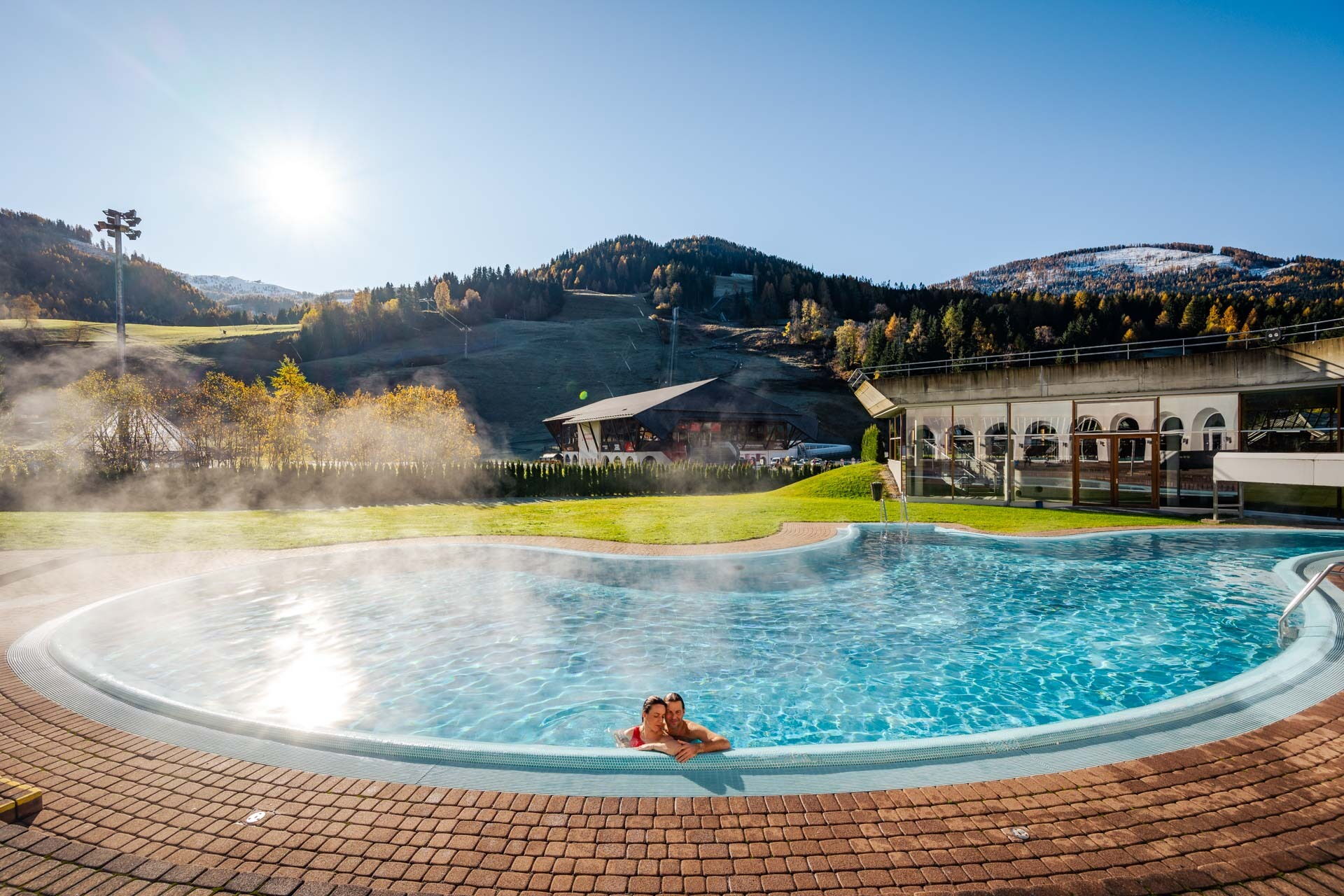 Couple enjoying a warm pool with a picturesque mountain backdrop and morning sunshine.