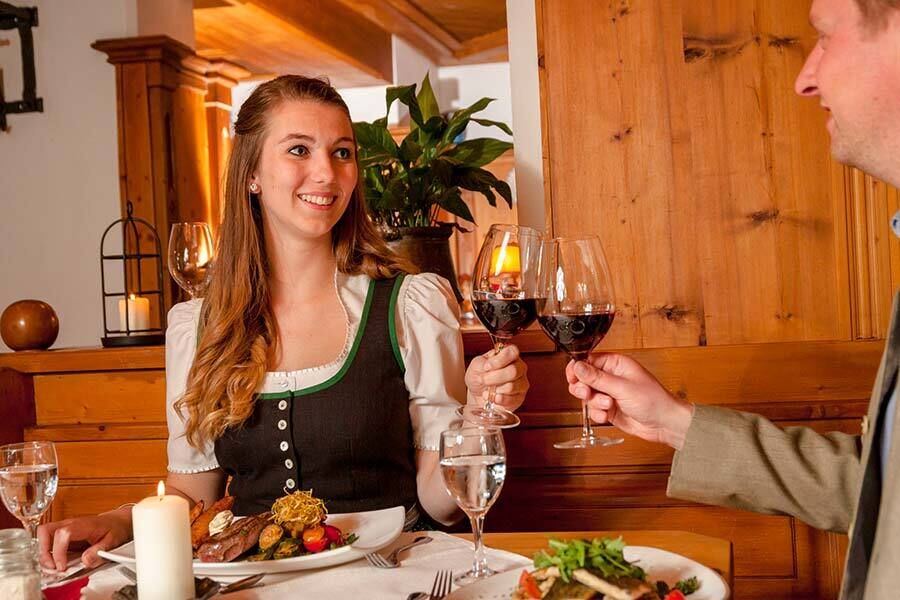 Two people clink glasses of red wine by candlelight at a festively laid table.
