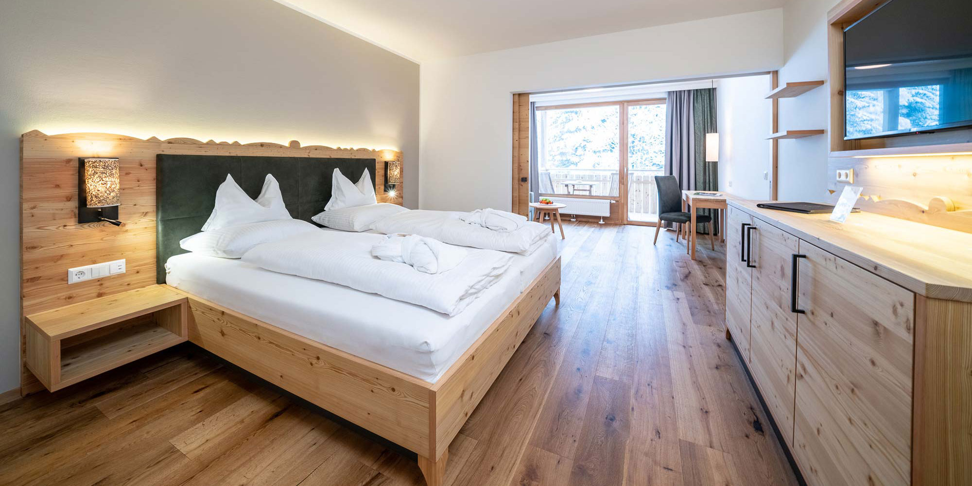 A large and bright hotel room with many wooden elements and a balcony.