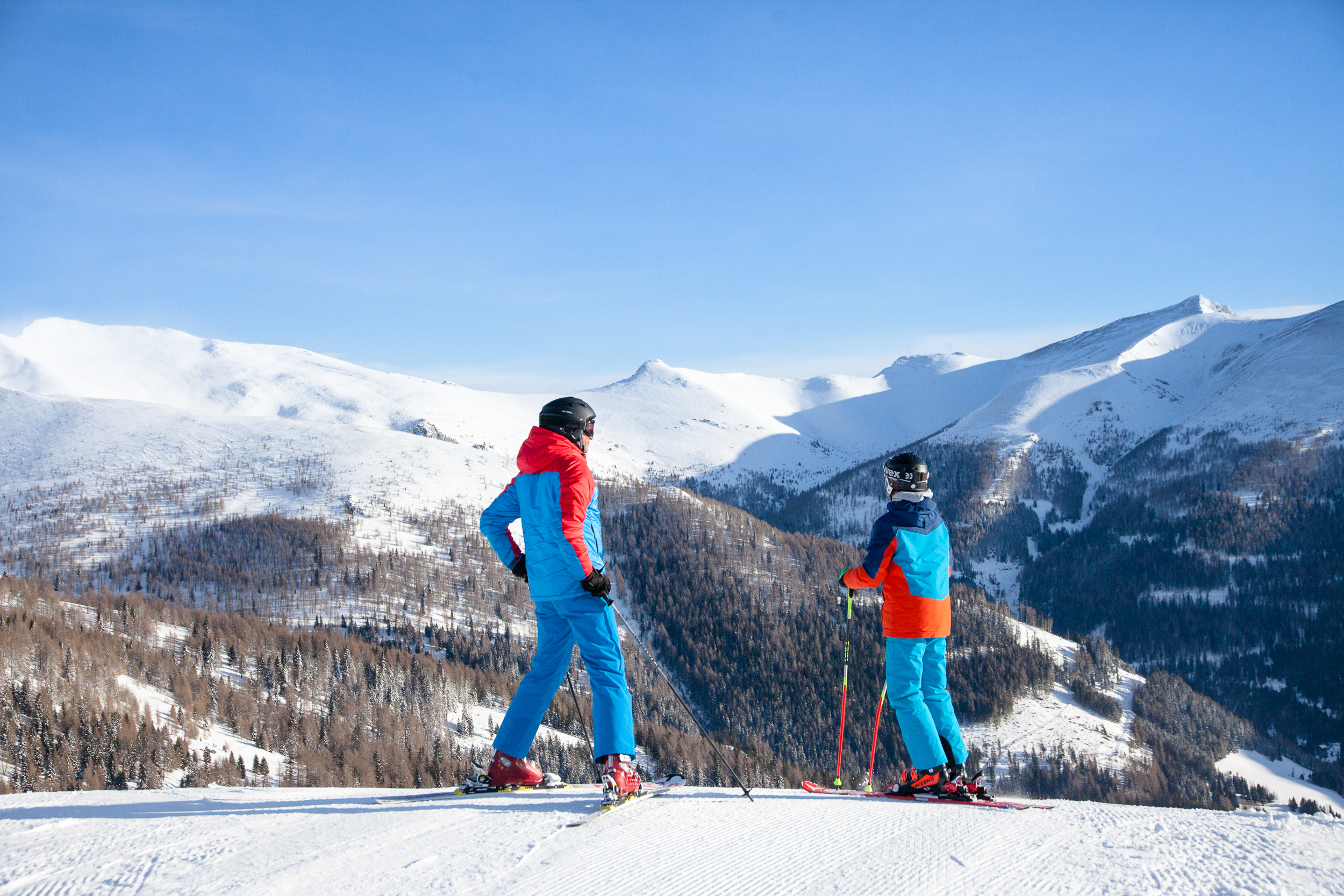 Vater und Sohn die ganz oben auf der Skipiste stehen und in die schneebedecken Berge sehen.