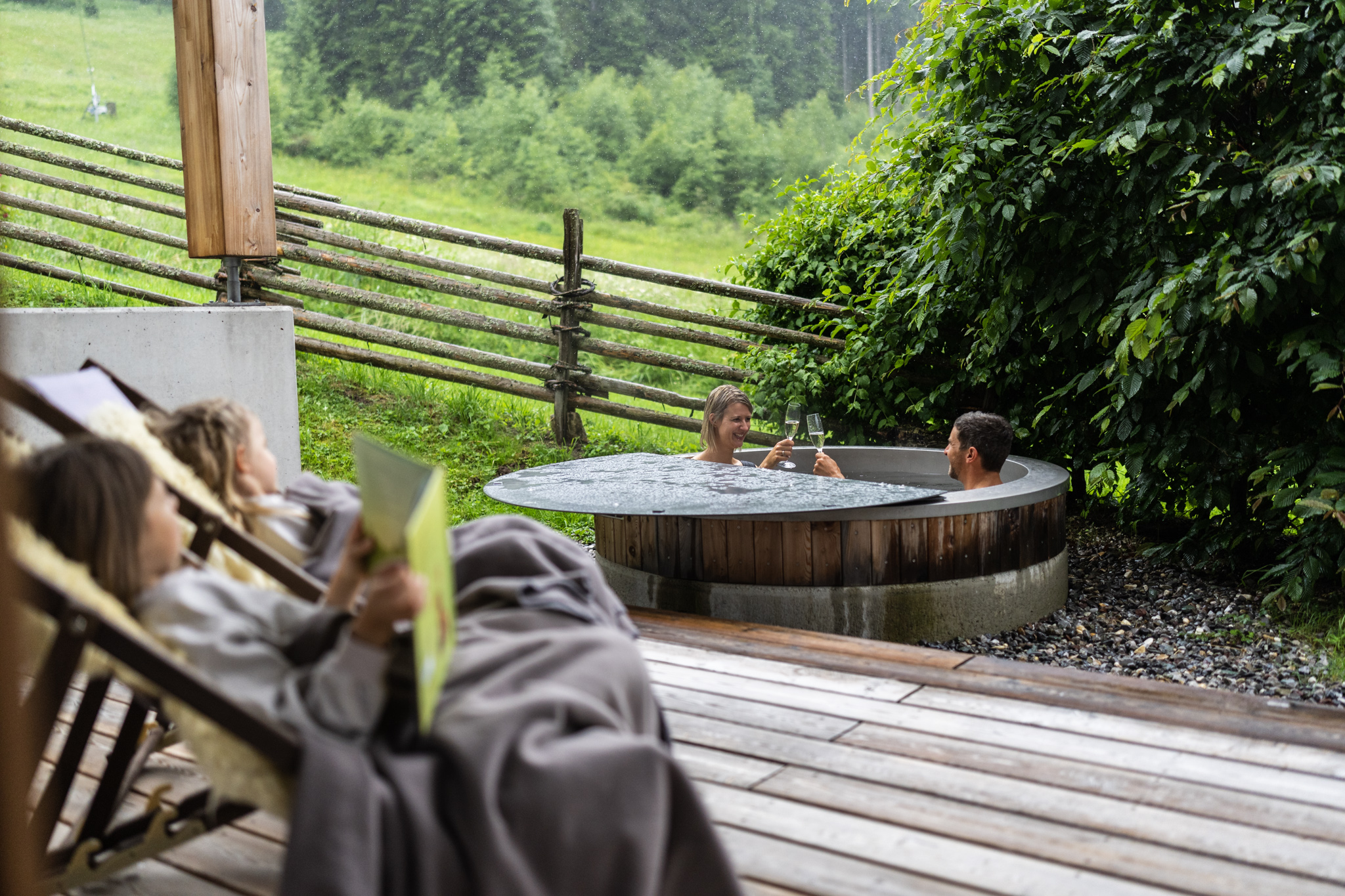 Two people enjoy a bath in the whirlpool, with a green background and deckchairs.