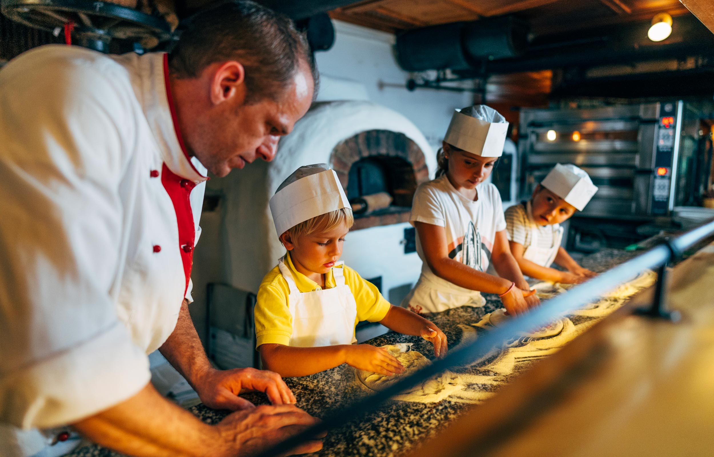 Il cuoco aiuta i bambini a impastare la pasta della pizza.